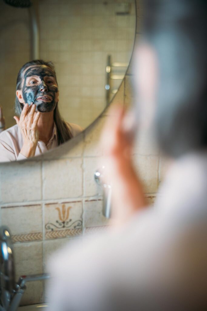 A senior woman applying a skincare face mask in a cozy bathroom setting, reflecting self-care and wellness.